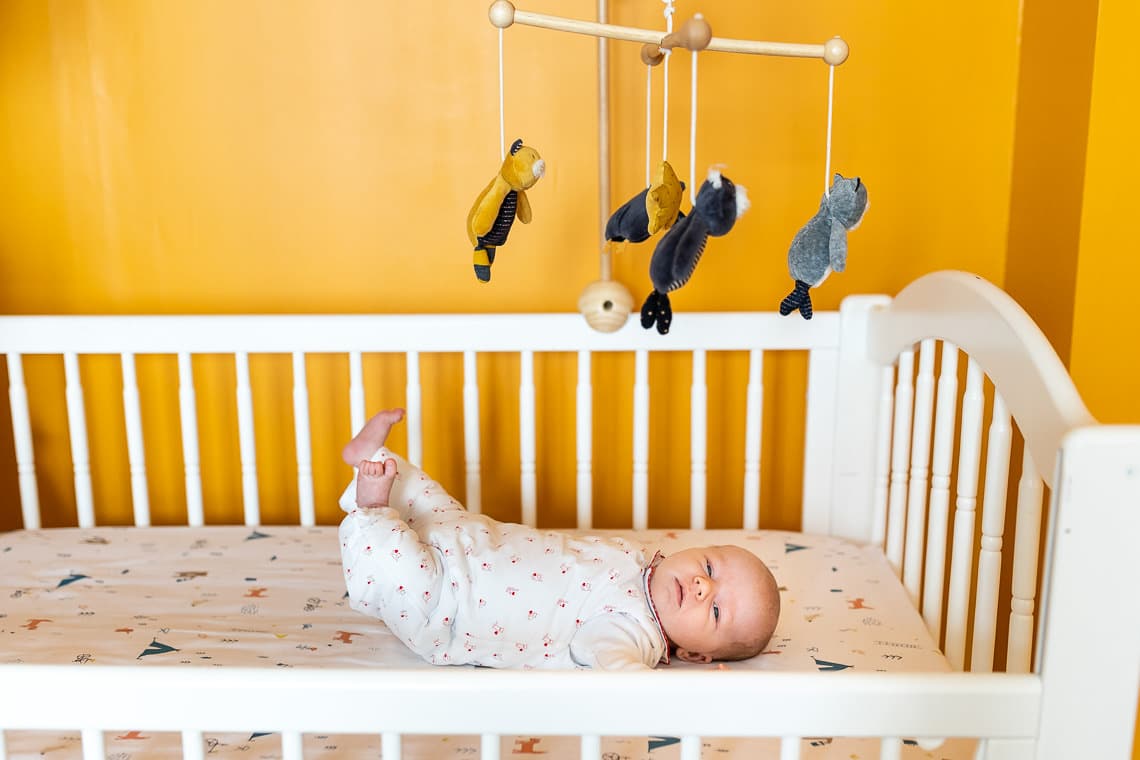 photo de bébé dans son berceau avec mur jaune et mobile oiseau